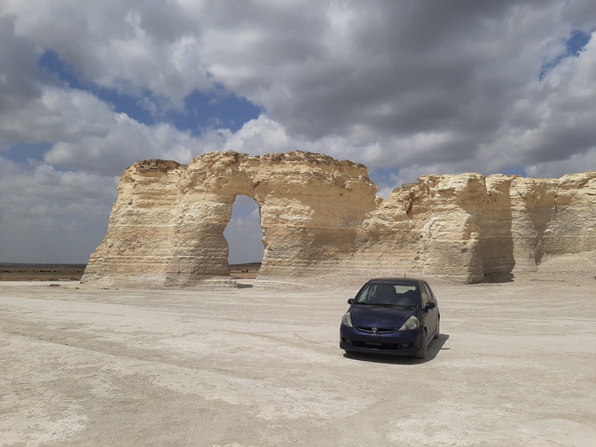 My Honda Fit at Monument Rocks, Kansas. A purple Honda Fit parked serenely in front of a large chalk rock formation called 'Monument Rocks' in Kansas, under billowing clouds, miles from anything and anyone else.